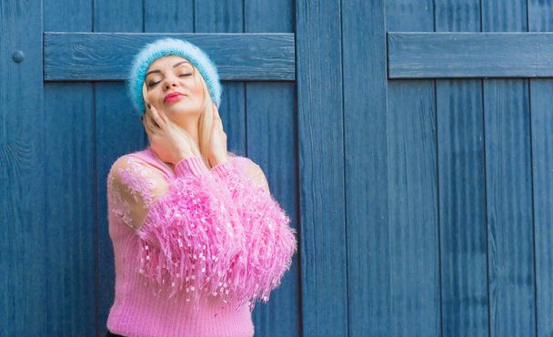 Mooie blonde vrouw met roze trui en blauwe wollen muts, winterseizoen. Vrouwenkleding, modieus concept - Foto, afbeelding