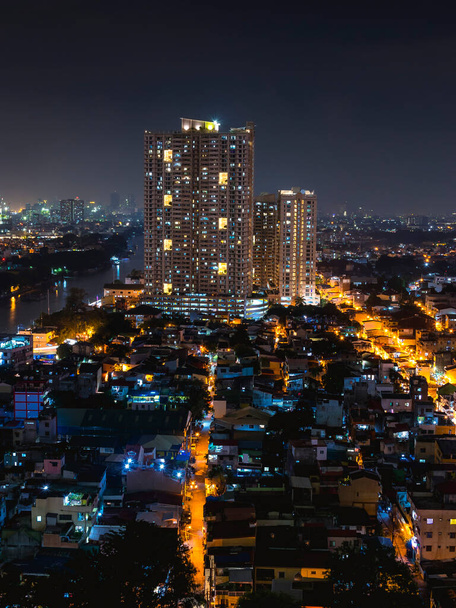 Mandaluyong, Metro Manila, Philippinen - Ein Paar Eigentumswohnungen überragen die nahe gelegenen Midrises. Nachtszene eines Stadtviertels am Fluss Pasig. - Foto, Bild