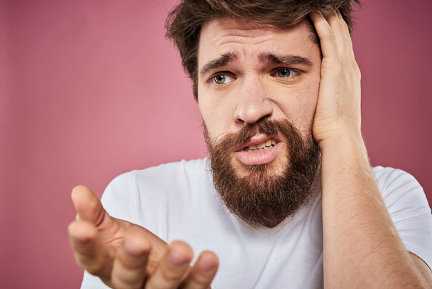 szakállas férfi fehér póló érzelmek elégedetlen arc kifejezés stúdió rózsaszín háttér - Fotó, kép