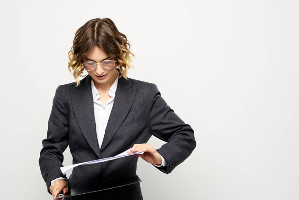 zakenvrouw in een pak met documenten in handen lichte achtergrond krullend haar kapsel - Foto, afbeelding