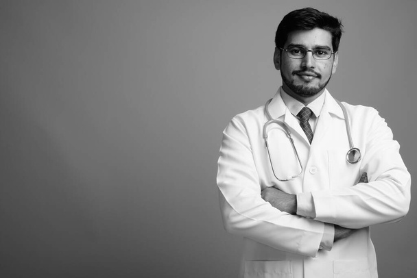 Молодой красивый бородатый персидский врач на сером фоне - Фото, изображение