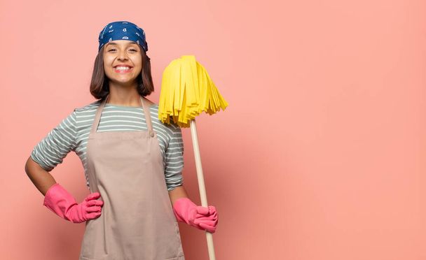 young woman housekeeper smiling happily with a hand on hip and confident, positive, proud and friendly attitude - Φωτογραφία, εικόνα