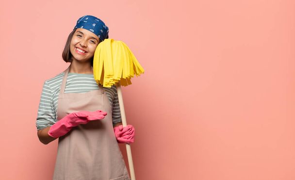 young woman housekeeper smiling cheerfully, feeling happy and showing a concept in copy space with palm of hand - Photo, image