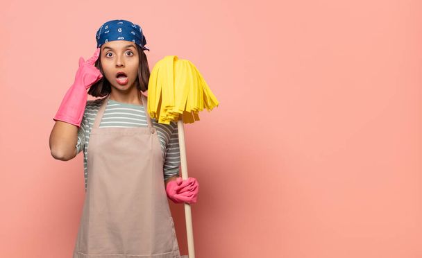 young woman housekeeper looking surprised, open-mouthed, shocked, realizing a new thought, idea or concept - Фото, изображение