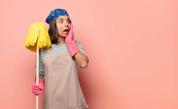 young woman housekeeper feeling happy, excited and surprised, looking to the side with both hands on face - 写真・画像
