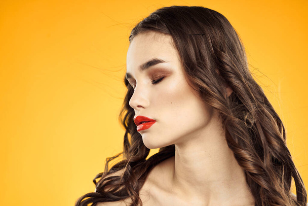 Красивая брюнетка голые плечи яркий макияж красные губы прическа крупным планом желтый фон - Фото, изображение