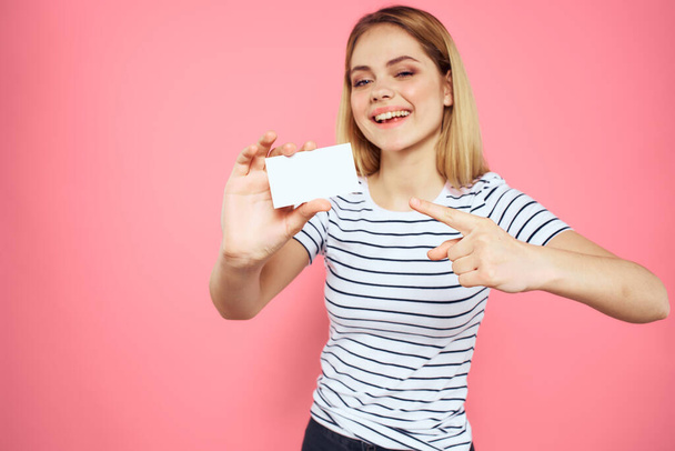 Nainen käyntikortti käsissään raidallinen T-paita vaaleanpunainen tausta Kopioi Space mainonta - Valokuva, kuva