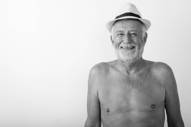 Estudio de tiro de hombre barbudo alto feliz sonriendo mientras usa sombrero sin camisa sobre fondo blanco - Foto, Imagen