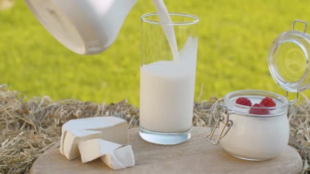 Крупным планом молоко наливается в стакан, сыр и йогурт с малиной на деревянной доске в саду в летний день. Камера медленно движется по ползунку - Кадры, видео