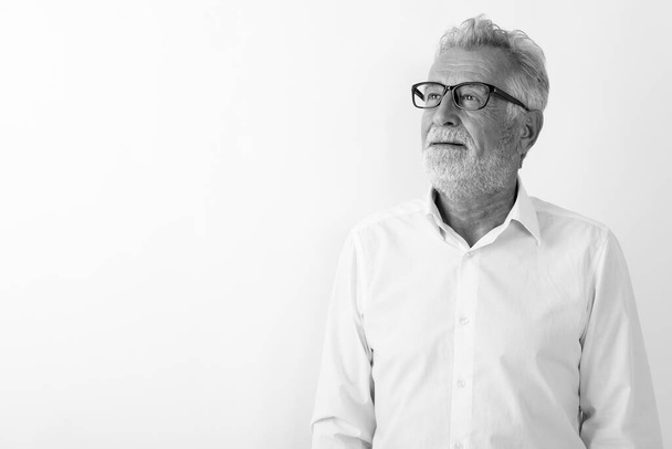 Studio shot of happy senior bearded man smiling and thinking with eyeglasses against white background - Photo, Image