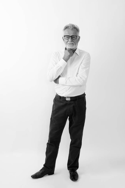 Full tělo záběr pohledný starší vousatý muž stojící při myšlení a nošení brýlí na bílém pozadí - Fotografie, Obrázek