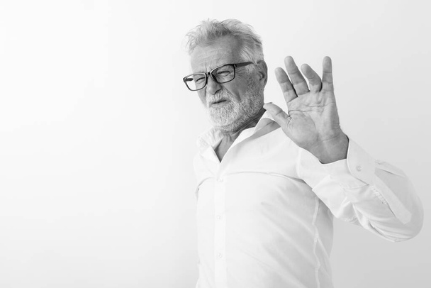 Studio zdjęcie starszego brodatego mężczyzny wyglądającego na zdegustowanego, pokazującego znak stopu i noszącego okulary na białym tle - Zdjęcie, obraz