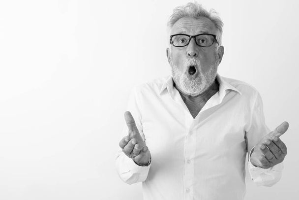 Studioaufnahme eines gutaussehenden, bärtigen Mannes mit offenem Mund, der schockiert aussieht, während er eine Brille vor weißem Hintergrund trägt - Foto, Bild