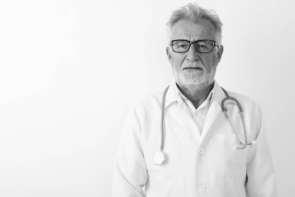 Studio shot of handsome senior bearded man doctor wearing eyeglasses against white background - Photo, image