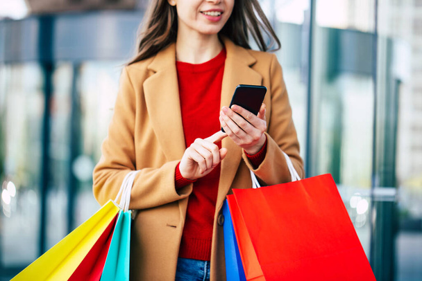 Stylish modern beautiful young woman with smart phone and shopping bags while she walking outdoor after mall - Foto, imagen