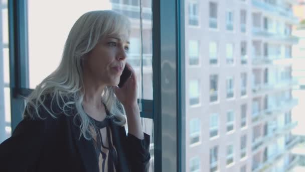 Ernstige middelbare leeftijd zakenvrouw staan in de buurt venster - Video