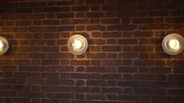 Three lights on a red brick wall from the interiors of a vegan restaurant - Πλάνα, βίντεο