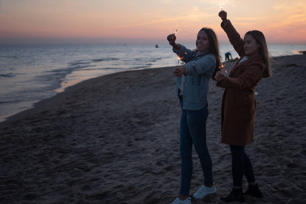 Two cheerful friends on the beach in the evening light sparklers. - Photo, Image