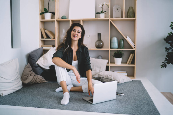 Portrait of cheerful caucasian female in casual wear resting at home on free time using laptop computer for browsing and communication, positive hipster girl looking at camera working on freelance at flat - Φωτογραφία, εικόνα