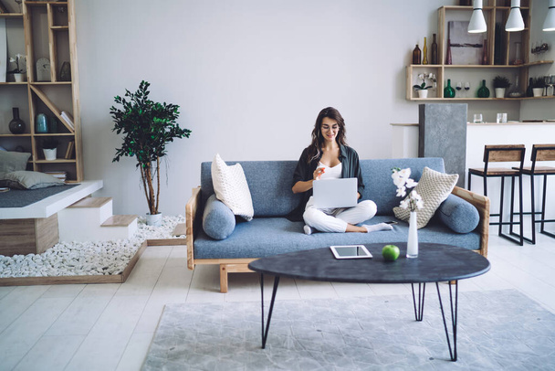 Smiling caucasian female in casual wear working remotely at home interior with modern designed room, positive millennial woman using laptop computer for browsing and communication in apartment - Valokuva, kuva
