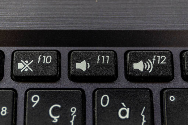 Un retrato de cerca de los botones de silencio, volumen arriba y volumen abajo en un teclado portátil. Las teclas físicas son negras con un icono blanco en ellas para mostrar lo que hace el botón. - Foto, imagen