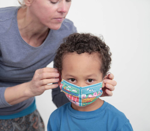 Mutter setzt Gesichtsmaske auf Kind Coronavirus Schutz auf weißem Hintergrund Archivfoto - Foto, Bild