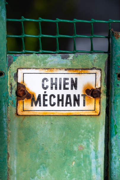 Roestig waarschuwingsbord geschreven in het Frans "Vervelende hond" op een oud versleten groen hek - Foto, afbeelding