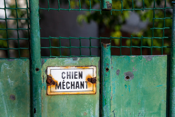 フランス語で書かれた錆びた警告サインで、古びた緑色の門の上に「汚い犬」と書いてあります。 - 写真・画像