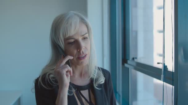 Сосредоточенная деловая леди средних лет стоящая у окна - Кадры, видео