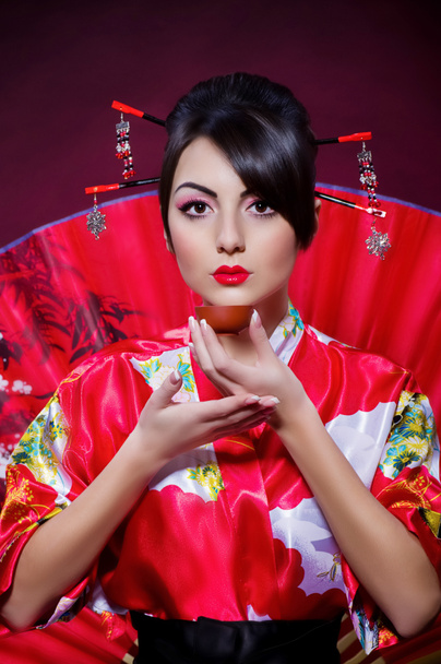 Nainen aasialaisessa puvussa järjestämässä teetilaisuutta
 - Valokuva, kuva