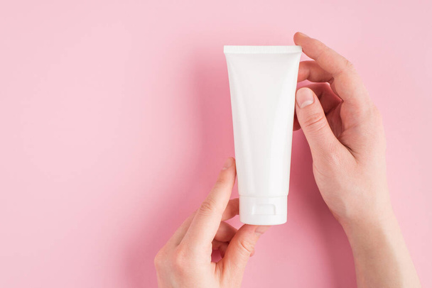 Skin moisturising concept. Top above overhead pov first person view photo of female hands holding white tube of cream isolated on pastel pink background with copyspace - Foto, Imagen