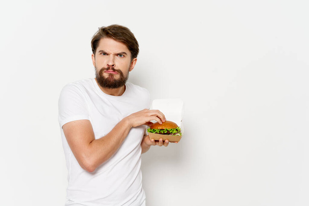  hombre adulto con una hamburguesa hizo pucheros sus labios y mira hacia adelante sobre un fondo aislado - Foto, imagen