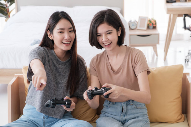 Dos adolescentes asiáticas son amigas íntimas con el pelo corto y largo sonriendo y jugando videojuegos en el dormitorio. Las mujeres jóvenes están disfrutando de actividades de ocio. - Foto, imagen