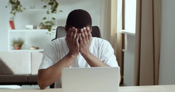 Portret van een vermoeide zwarte man Afrikaanse student die thuis naar een laptop kijkt. Afro Amerikaanse freelancer vindt stress leest slecht nieuws houdt hoofd met zijn handen in shock, verliest baan - Video