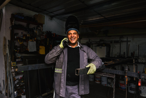 Foto de hombre con guantes especiales trabajando en la herrería haciendo un descanso para usar su teléfono. - Foto, imagen