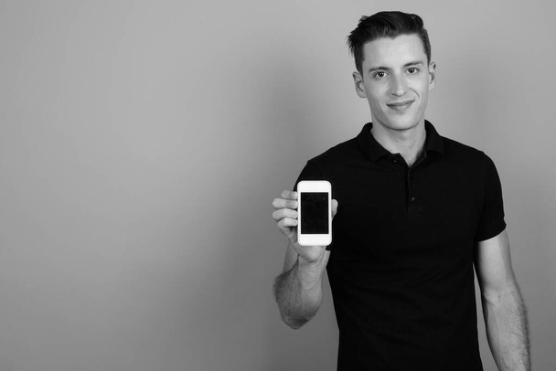 Junger schöner Mann mit Handy vor grauem Hintergrund - Foto, Bild