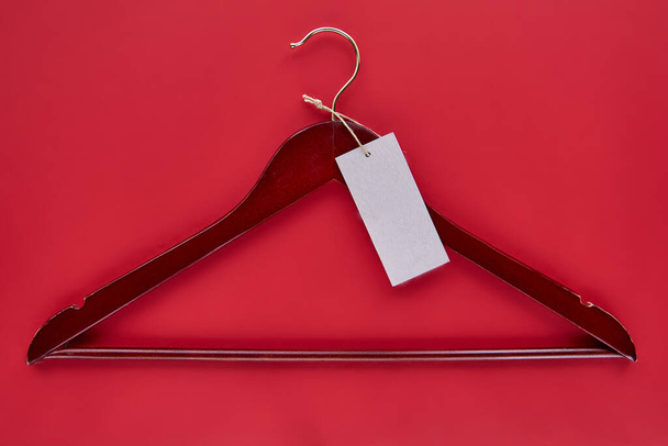 Roter Kleiderbügel aus Holz mit schwarzem Papieretikett isoliert auf rotem Papierhintergrund. Nahtlose Muster-Attrappe, um Ihr Design zu platzieren. Banner zum Schlussverkauf am Black Friday - Foto, Bild