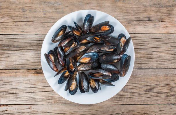 Many sea mussels in shells on a white plate on an old wooden background. View from above - Photo, Image