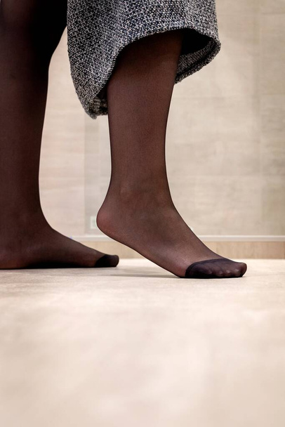 Portret stopy stojącej na czubku czarnej rajstopy dziewczyny podciągającej spódnicę. Nylon jest wzmocniony u stóp.. - Zdjęcie, obraz
