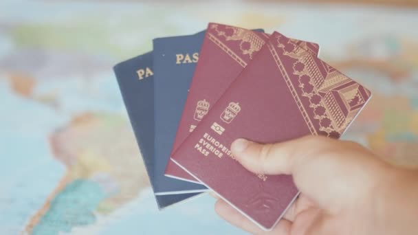 Mano sosteniendo pasaportes suecos y americanos frente a un colorido mapa del mundo - Metraje, vídeo