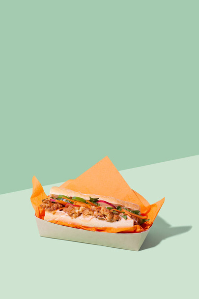 Vietnamese Banh Mi sandwich with roasted cauliflower and pickled veggie in takeaway packaging box on green background with copy space.Restaurant food delivery concept - Фото, зображення