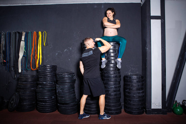 Athletes pregnant woman and husband posing in gym near sports equipment. Active sports pregnancy. Workout together during pregnancy. Pregnant woman with male exercising. Ukraine, Kiev October 11, 2020 - Photo, Image
