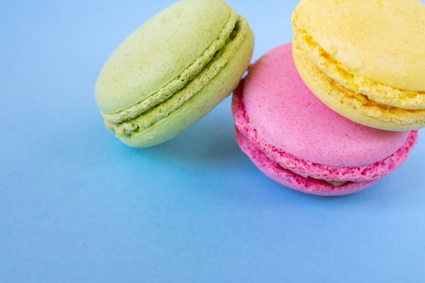 Yellow, pink and green macarons in the corner on blue background. Traditional french almond biscuits - Zdjęcie, obraz