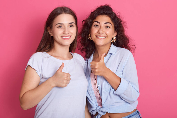 Portrait of nice looking attractive lovely fascinating cheerful dark haired ladies showing two thumbs up isolated over bright rose background, smiling women look at camera, wear casual shirts. - Фото, зображення