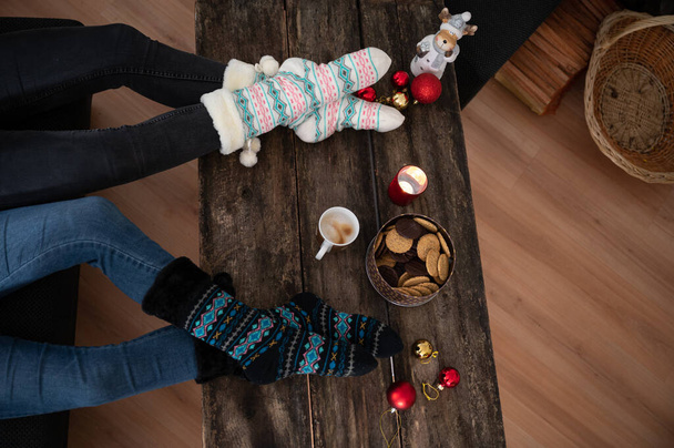 Вид зверху на дві жінки в теплих святкових носках, що сидять чашку кави та печива на сільському дерев'яному столі
. - Фото, зображення