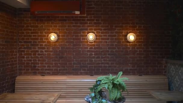 Mesas, sillas y tres luces en una pared de ladrillo rojo de un restaurante vegano - Imágenes, Vídeo