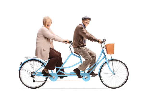 Elderly man and woman riding a blue tandem bicycle and looking at camera isolated on white background - Valokuva, kuva