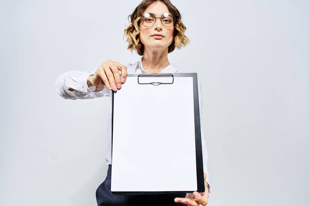 Деловая женщина с папкой с белыми документами в руке на светлом фоне и моделью очков в стиле прически - Фото, изображение