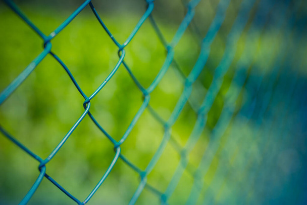 Заборная проволока, забор с металлической сеткой в перспективе на зеленом размытом фоне природы - Фото, изображение