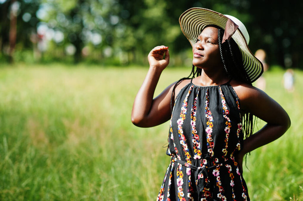 Portrait of gorgeous african american woman 20s in summer hat posing at green grass in park. - Фото, изображение